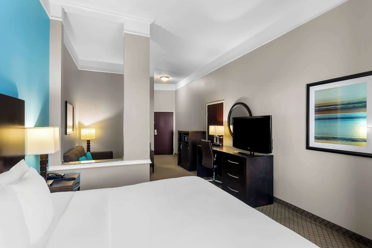 A hotel room with a bed, a desk with a computer, a TV, and a painting on the wall.