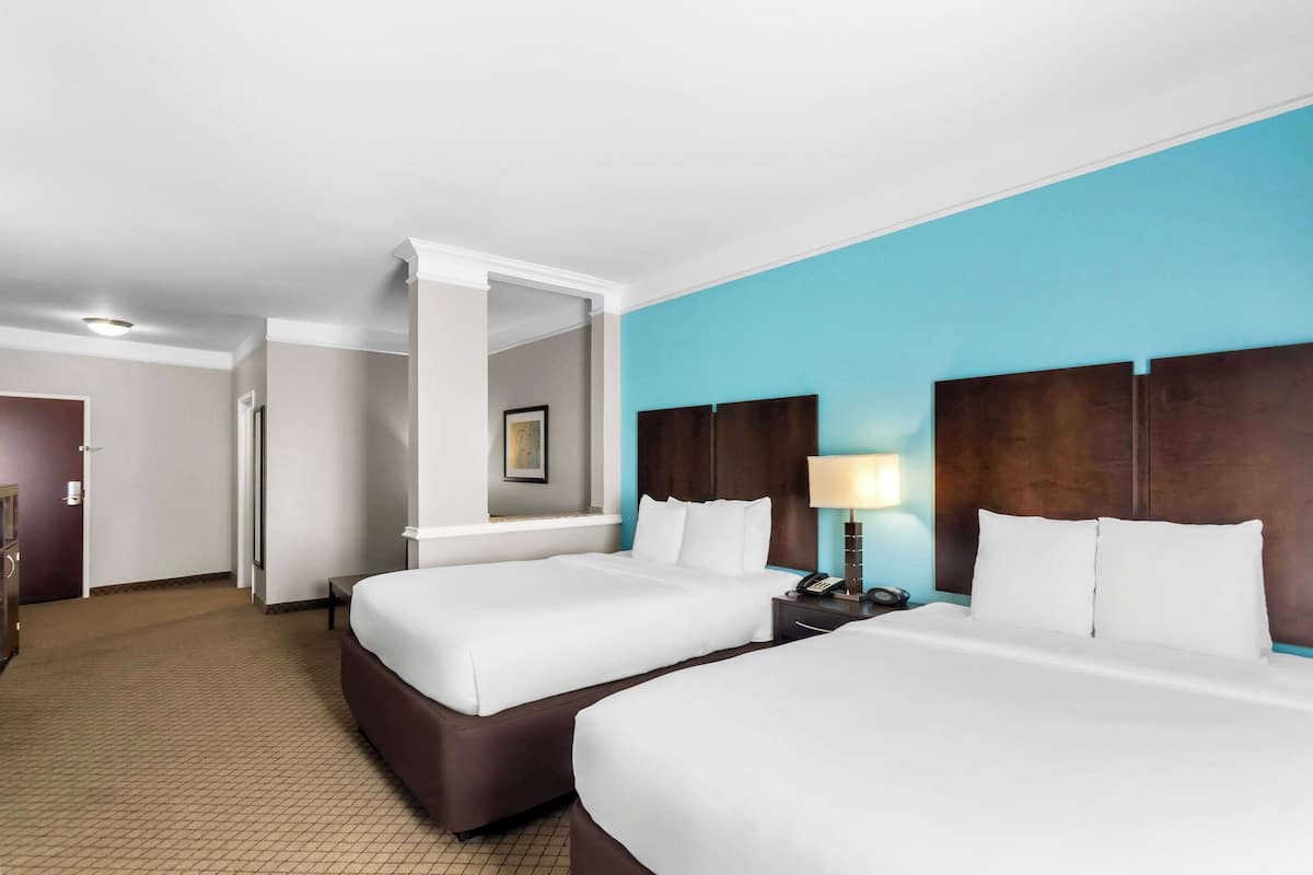 A hotel room with two beds, a nightstand, a lamp, and a mirror.