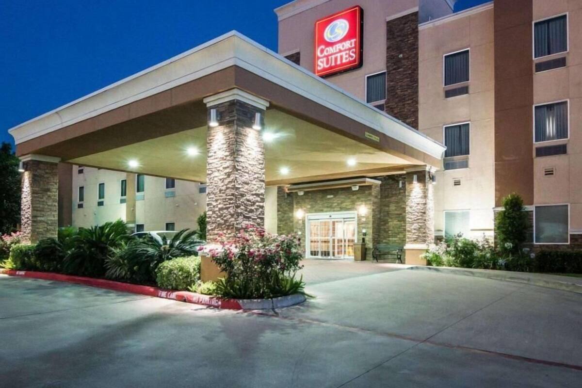 A Comfort Suites hotel with a covered entrance, stone pillars, and a red sign.