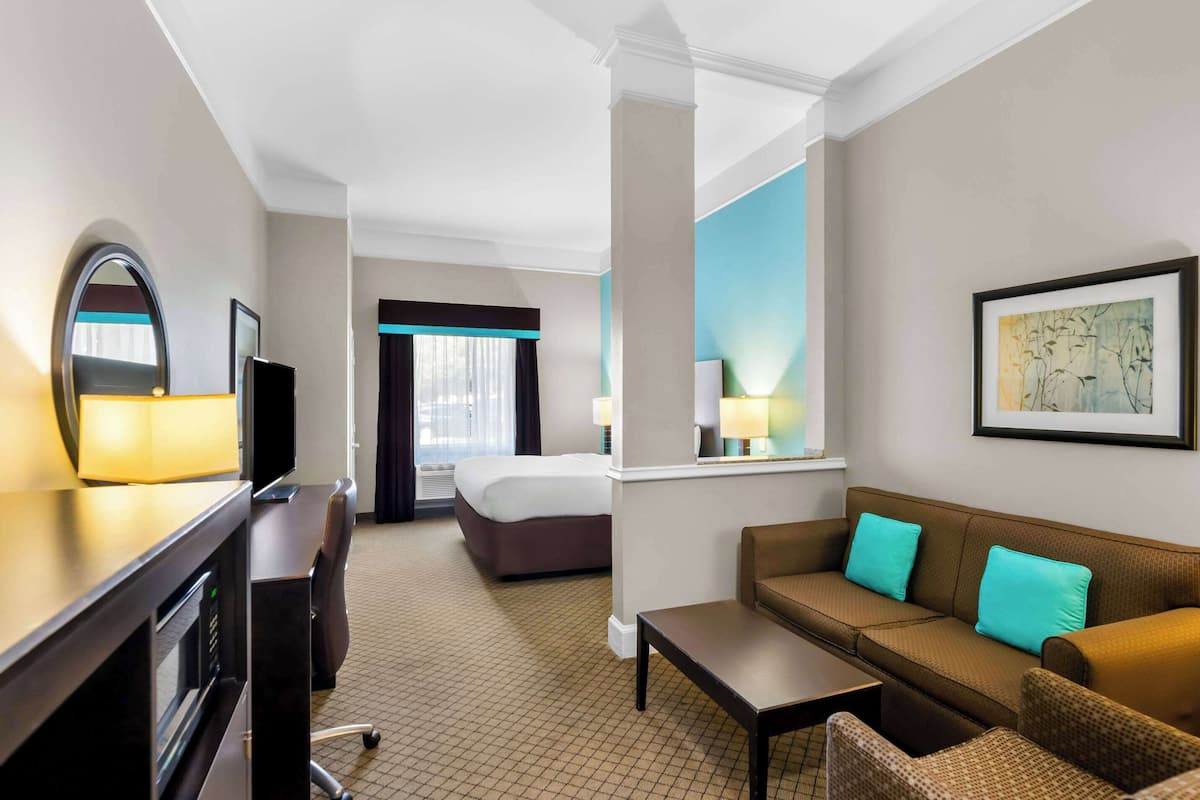 A hotel room with a bed, a desk with a computer, a sofa, and a window with curtains.