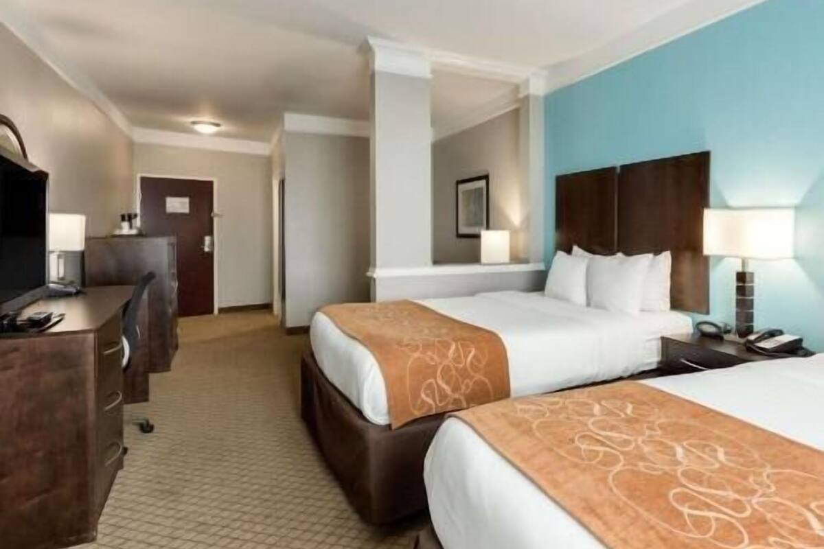 A hotel room with two beds, a desk, a chair, and a TV.