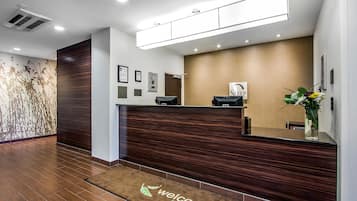 A reception area with a wooden reception desk, a welcome mat, and framed certificates on the wall.