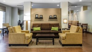 Eine moderne Lobby mit einem braunen Sofa, zwei Sesseln, einem Couchtisch und einem Wandregal mit gerahmten Bildern.