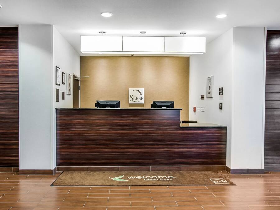 A reception desk with a 'Sleep Inn & Suites' sign, a Dell computer, and a welcome mat.