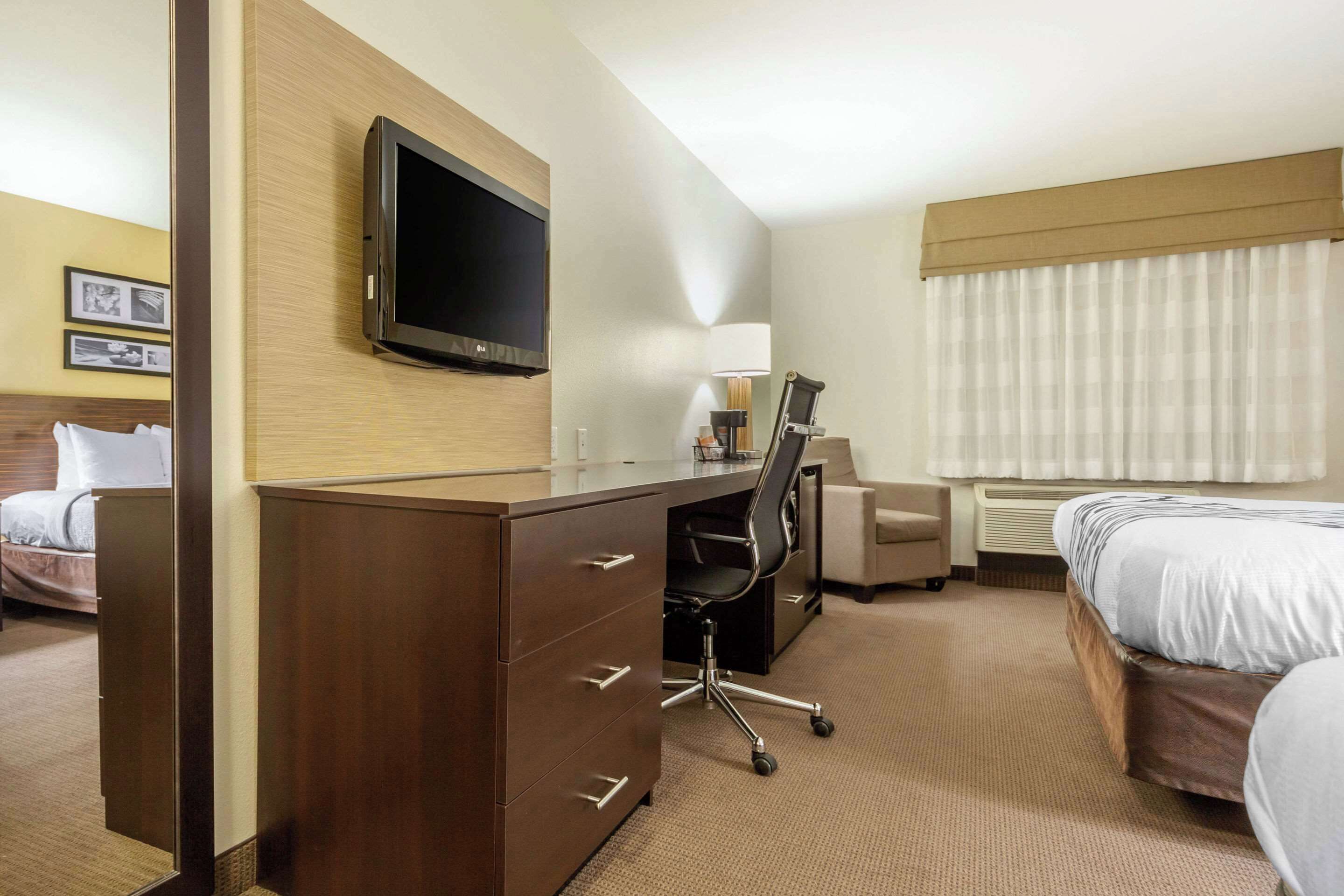 A hotel room with a bed, a desk with a chair, a television, and a window with curtains.