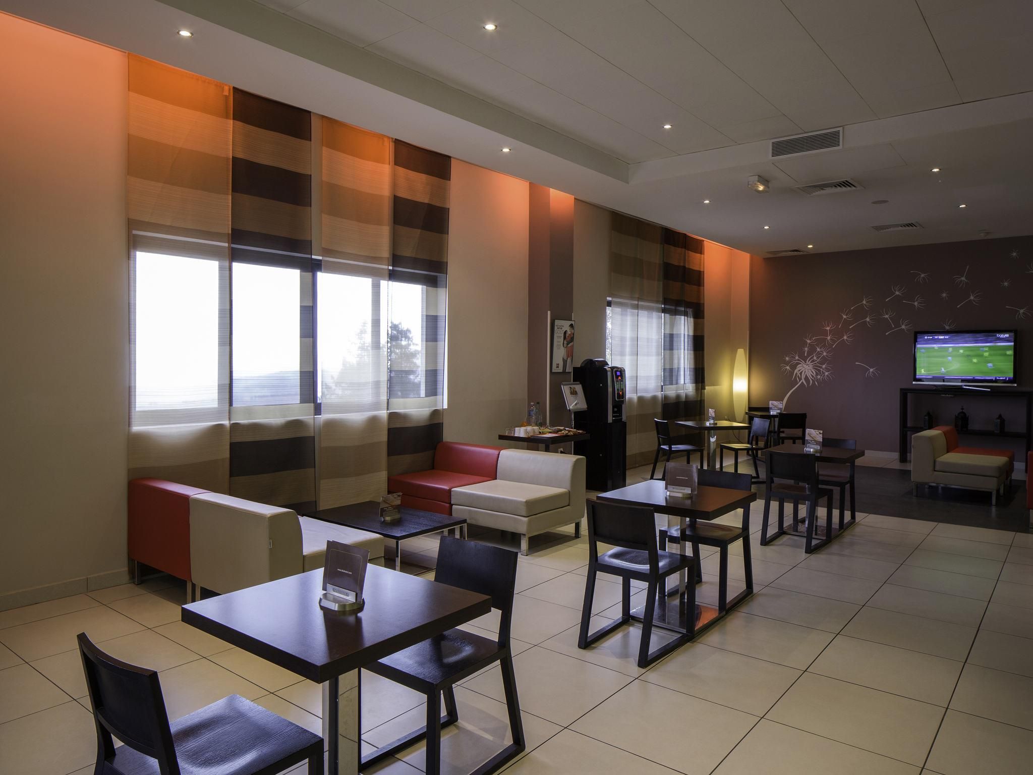 Un vestíbulo de hotel con zonas de estar, una máquina de café, un televisor y una chimenea.