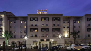 Et hotel med en markant indgang, flere etager og en parkeringsplads med biler.