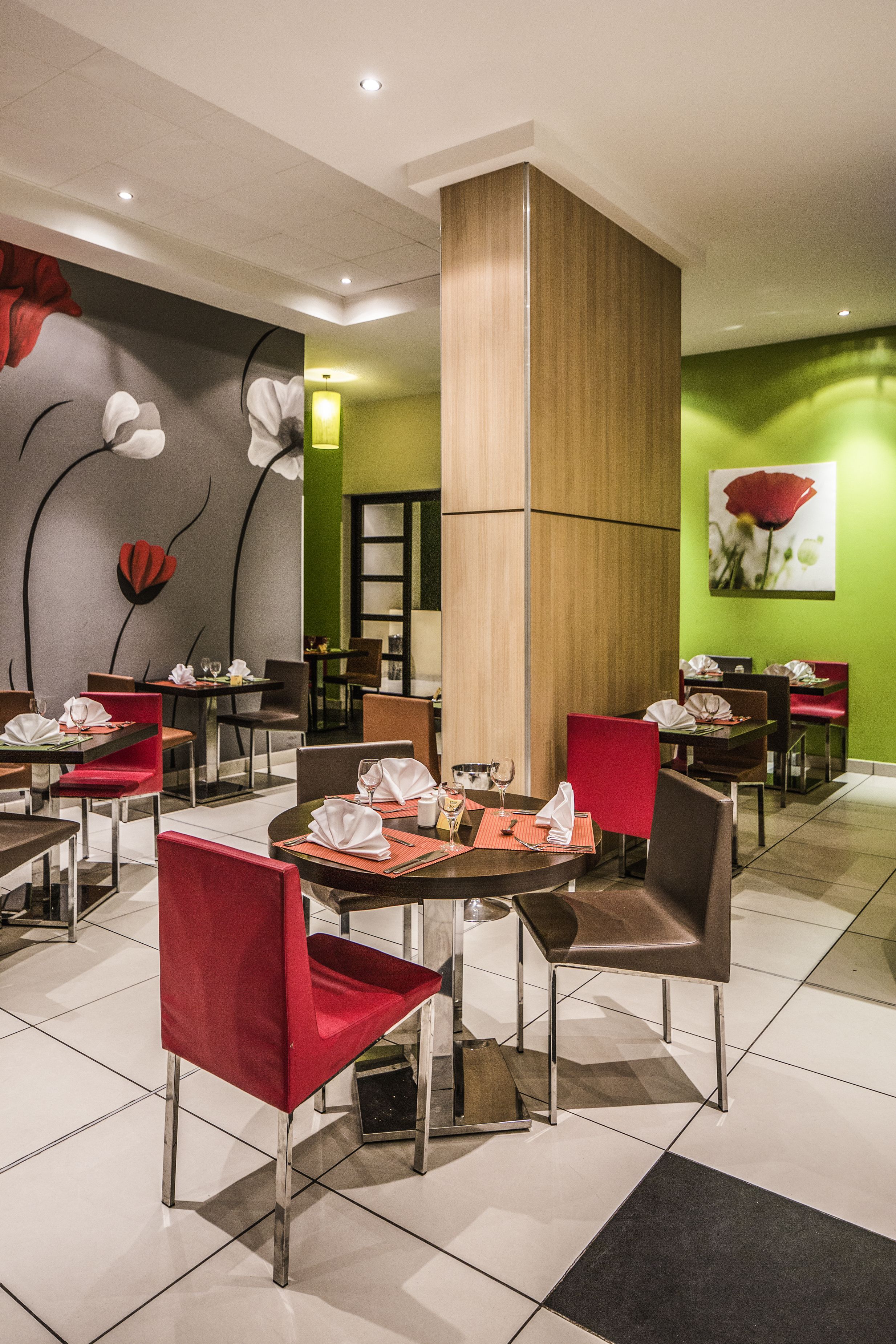 A modern dining area with red chairs, round tables, and a green accent wall.