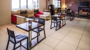 Un hall d’hôtel moderne doté d’un espace repas, de différents coins salon et d’un grand téléviseur à écran plat fixé au mur.
