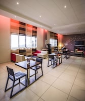 Un moderno vestíbulo de hotel con zona de comedor, arreglos para sentarse y un televisor de pantalla plana grande en la pared.