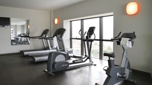 Une salle de sport équipée de tapis de course, de vélos elliptiques et dotée d’une grande fenêtre offrant une vue sur la ville.