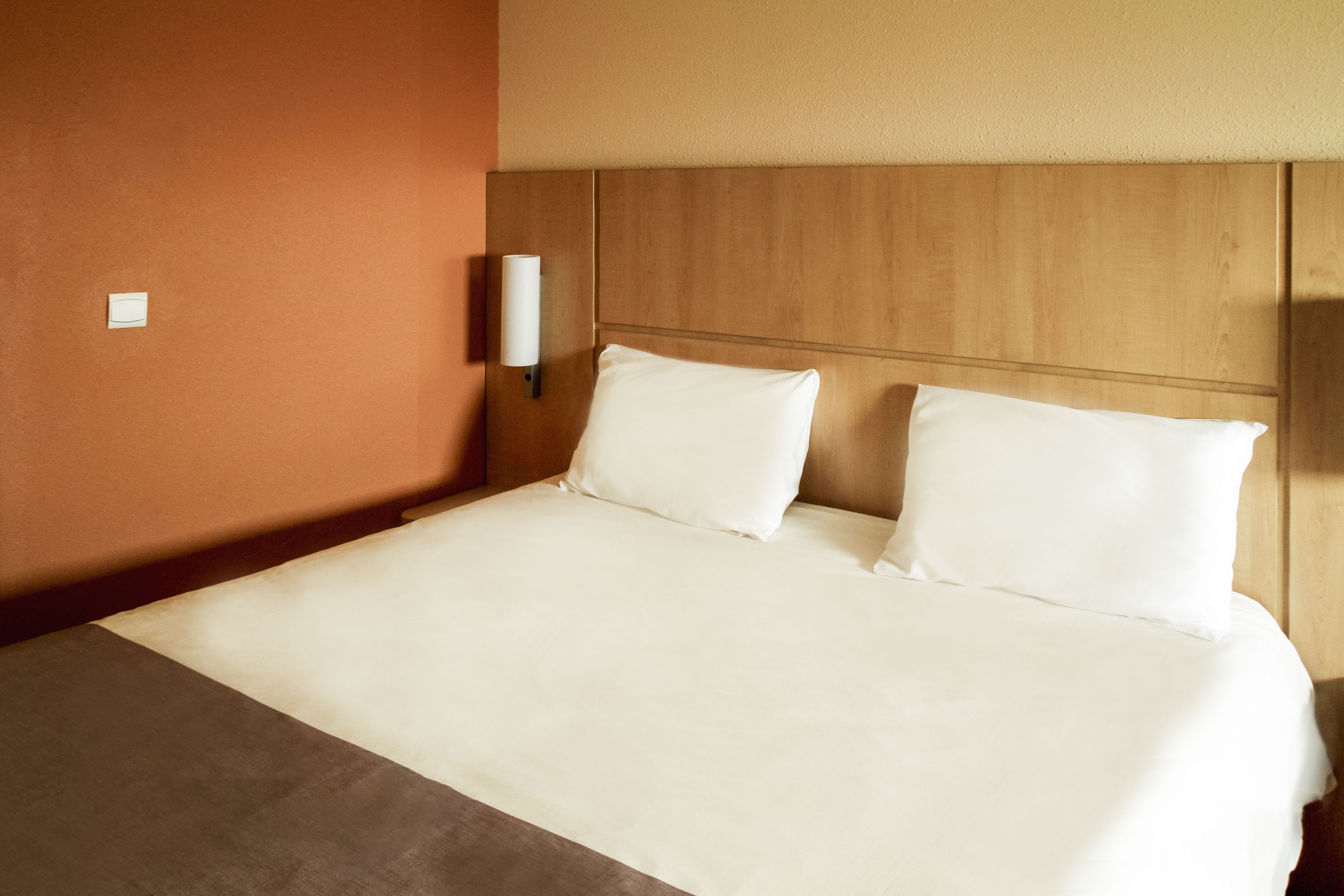 Una habitación de hotel con una cama grande, cabecero de madera y una lámpara fijada a la pared.