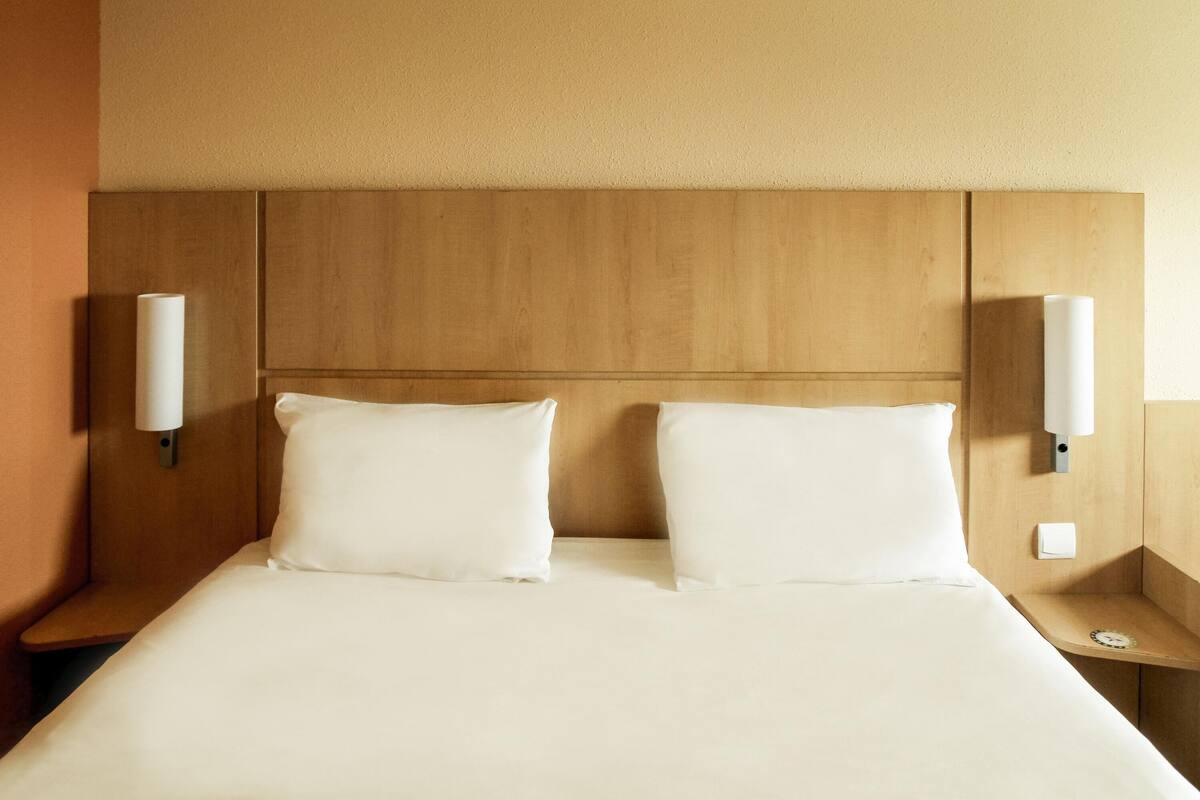 A hotel room with a wooden headboard, two white pillows, and bedside lamps.