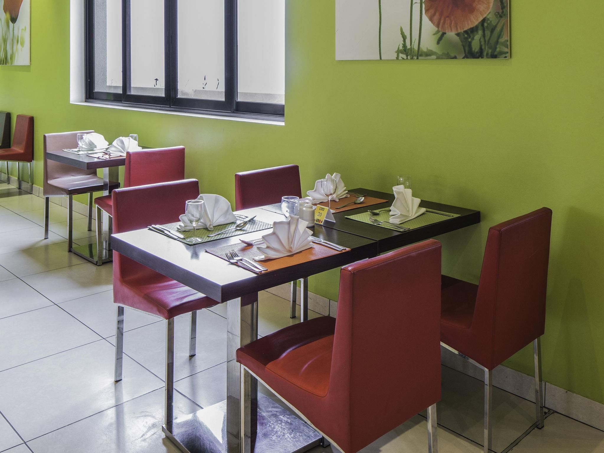 Un restaurant amb taules preparades per dinar, cadires vermelles i una paret verda.
