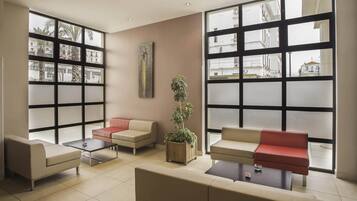 A modern lounge area with large windows, comfortable seating, and a potted plant.