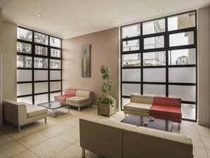 A modern lounge area with large windows, comfortable seating, and a potted plant. - ibis Constantine (Constantine)