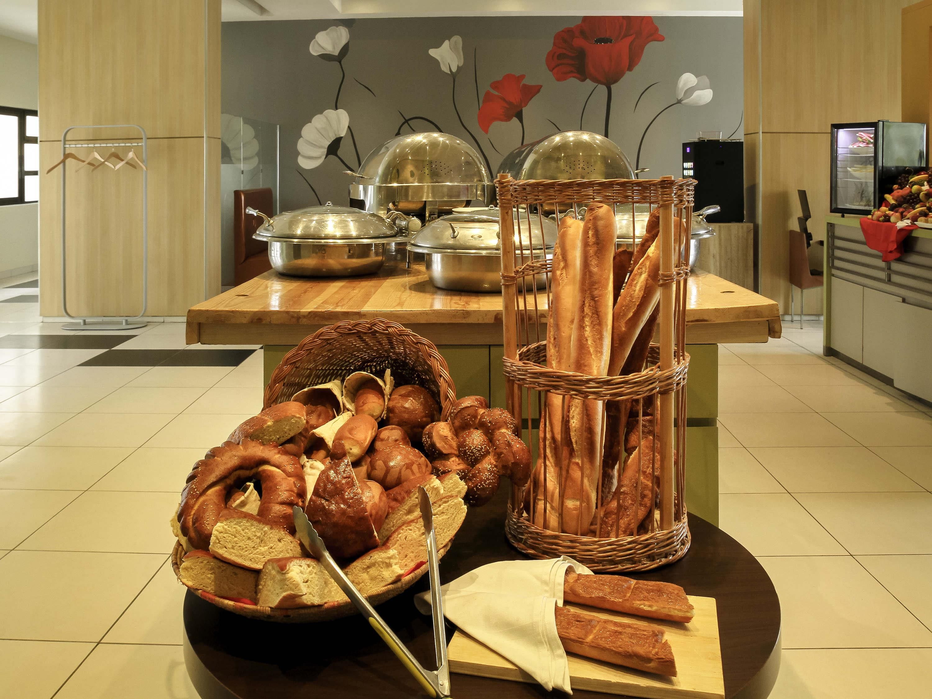Una mesa de buffet con panes y pasteles diversos, una cesta de mimbre y un recipiente metálico.