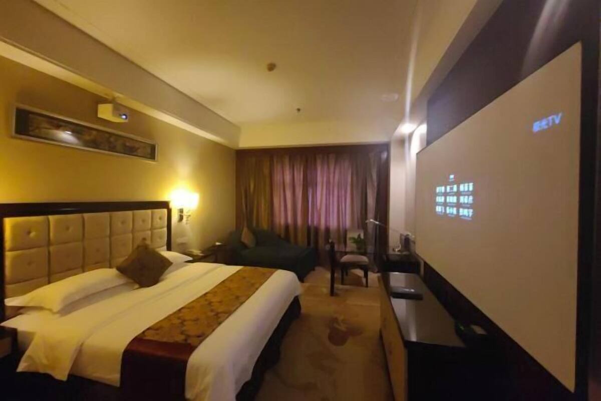 Een hotelkamer met een bed, een bureau, een stoel, een televisie en een scherm aan de muur.