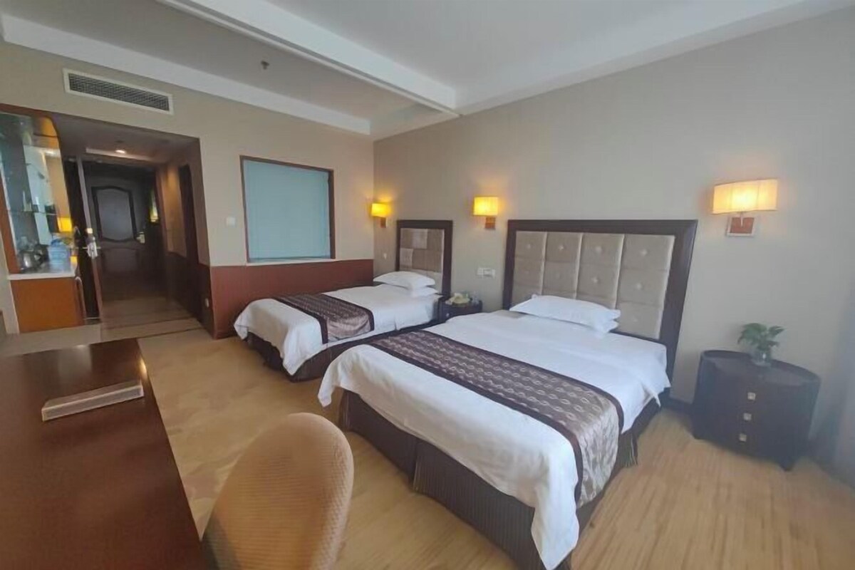 Hotellihuone, jossa on kaksi sänkyä, työpöytä, tuoli ja pieni sivupöytä.