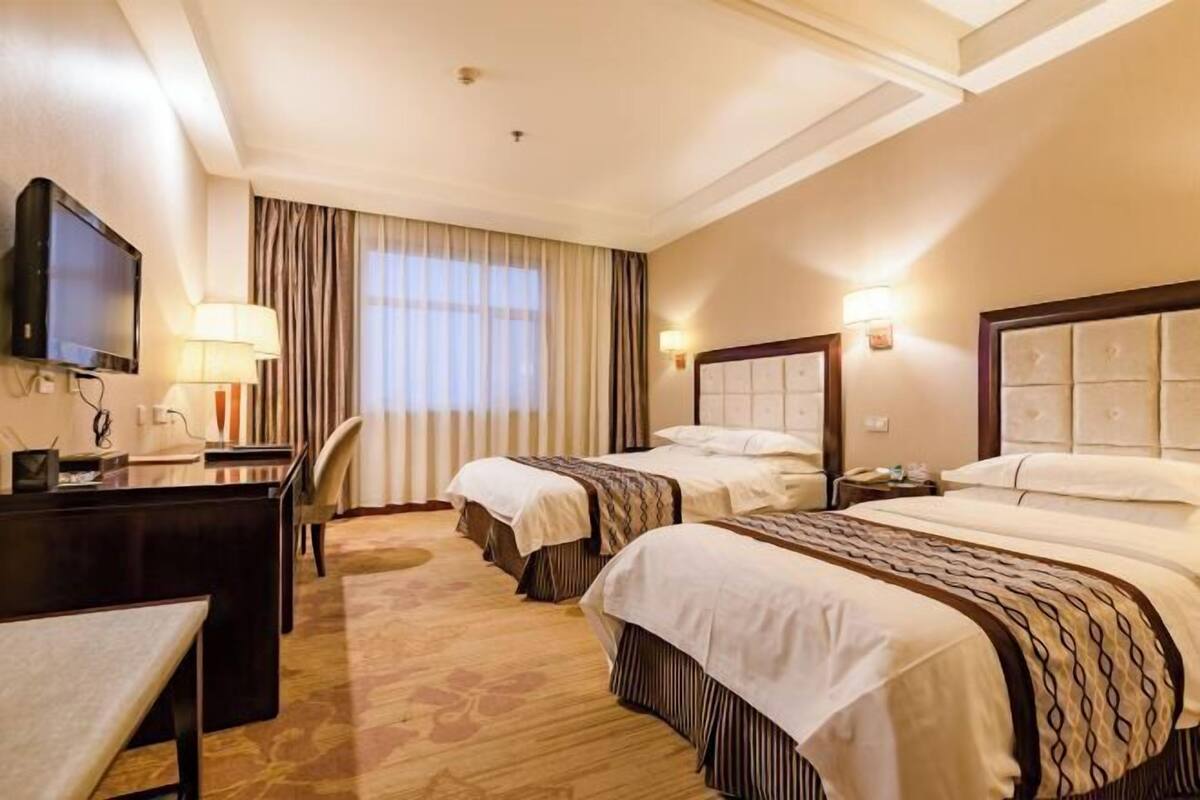 Een hotelkamer met twee bedden, een bureau, een televisie en een raam met gordijnen.