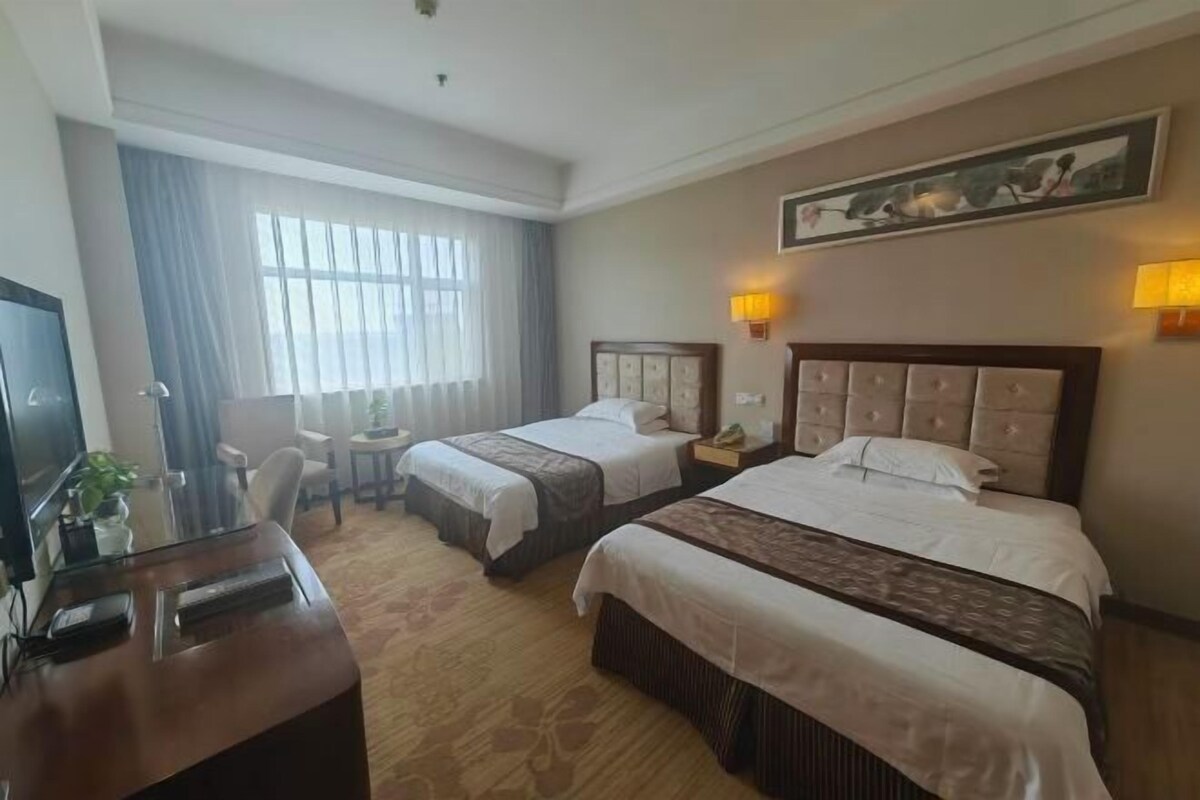 Hotellihuone, jossa on kaksi sänkyä, työpöytä, televisio ja ikkuna, jossa on verhot.