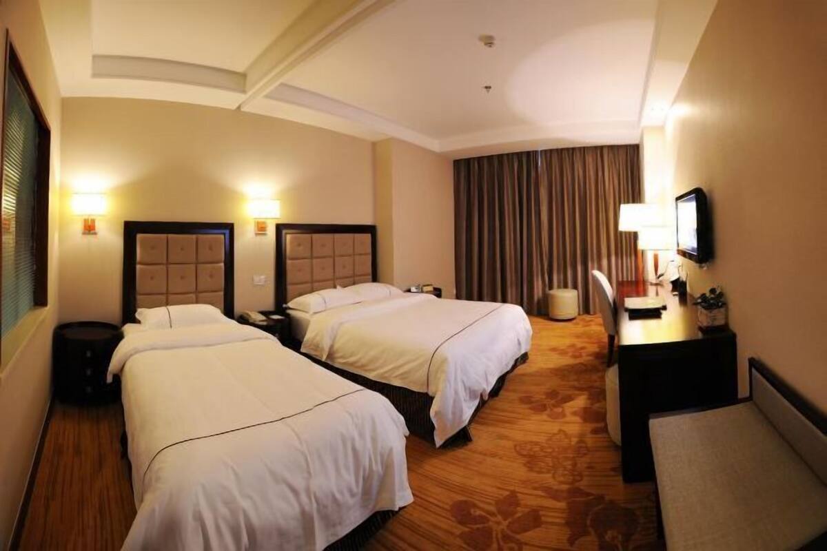 Een hotelkamer met twee bedden, een bureau, een stoel, een televisie en een raam met gordijnen.