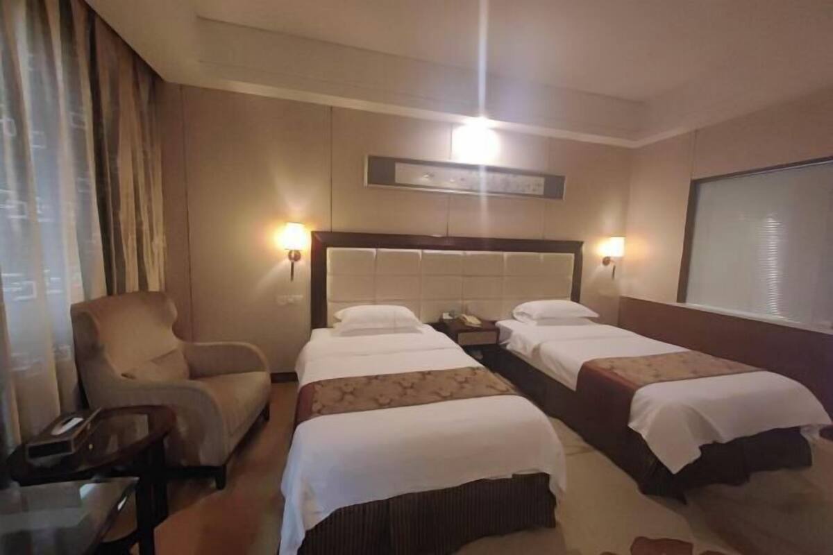 Een hotelkamer met twee bedden, een stoel, een bureau en een groot raam.