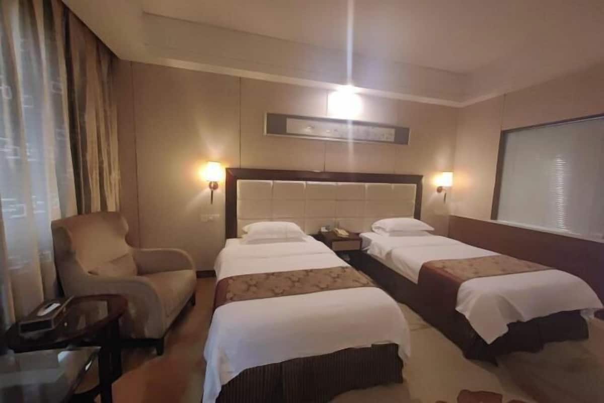 A hotel room with two beds, a chair, a desk, and a large window.