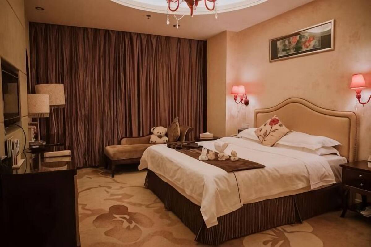 Een hotelkamer met een groot bed, een bureau, een stoel, een knuffelbeer en een lamp.