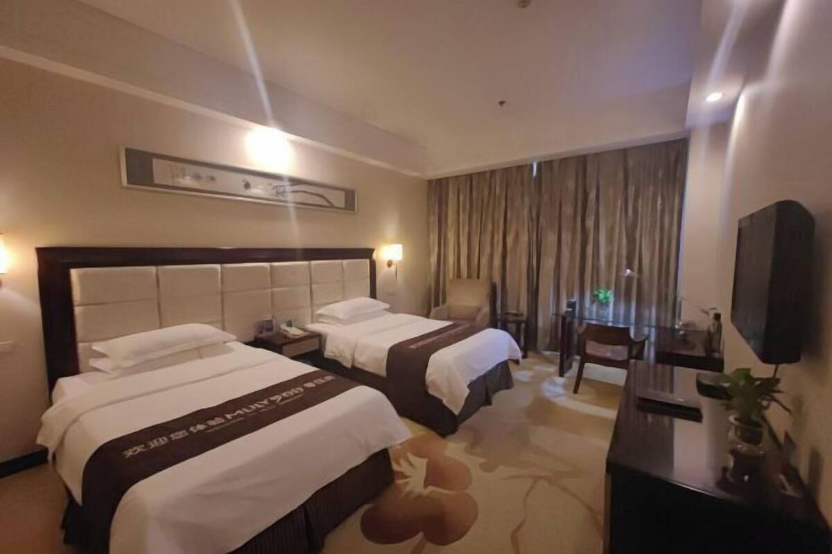 Een hotelkamer met twee bedden, een bureau, een stoel, een televisie en een groot raam met gordijnen.