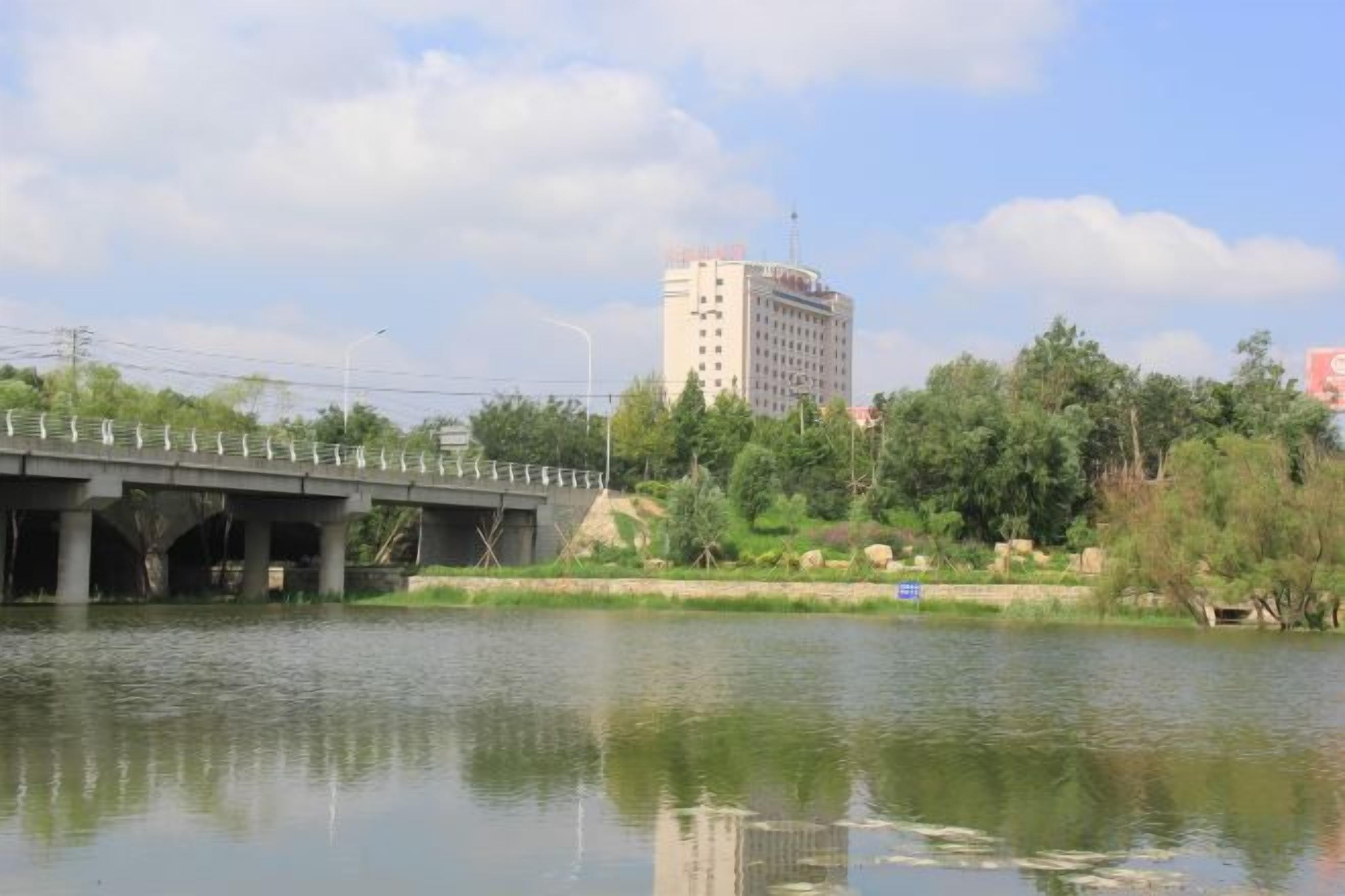 Un río con un puente, árboles y un edificio al fondo.