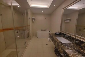 Ein modernes Badezimmer mit einer Duschkabine aus Glas, einer freistehenden Badewanne und einem Marmor-Waschtisch mit großem Spiegel.