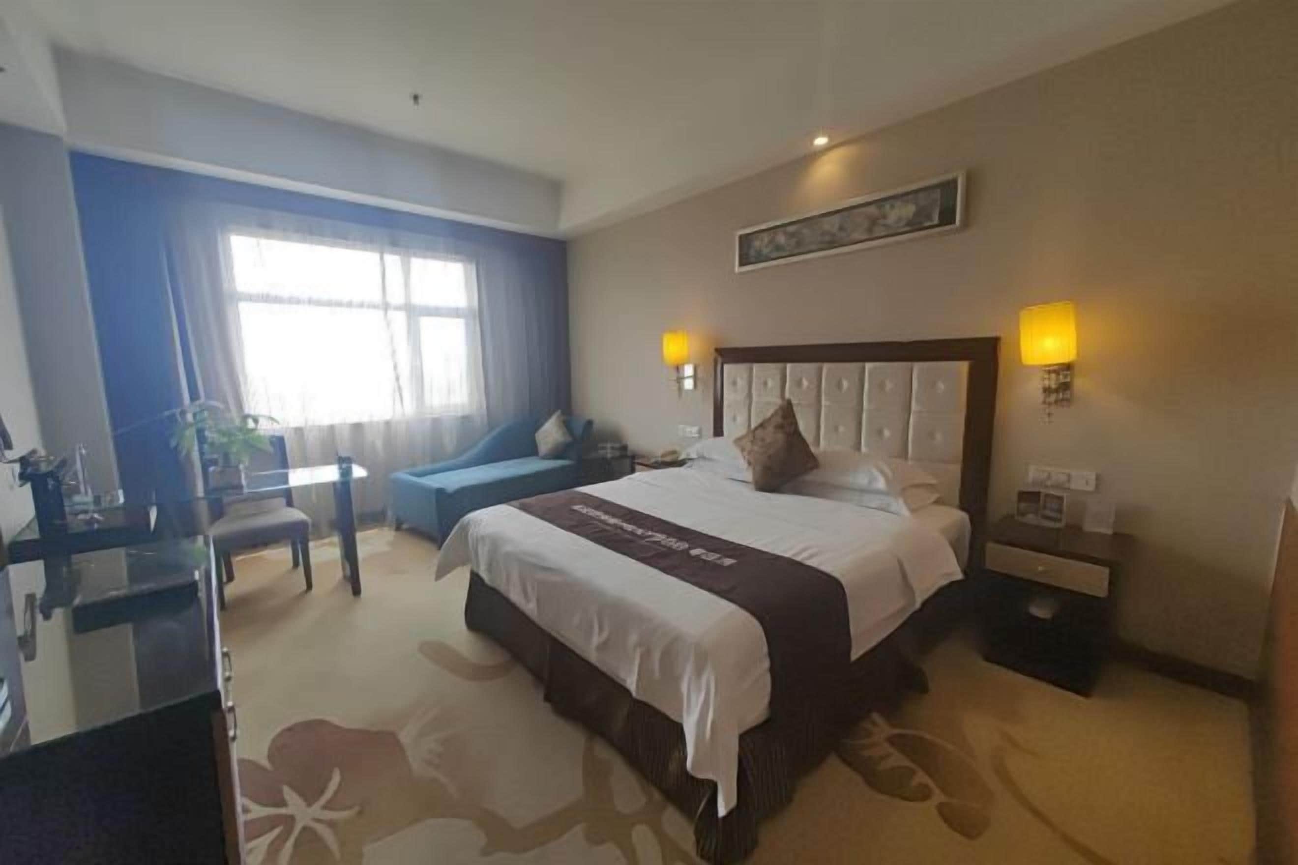 Ein Hotelzimmer mit einem großen Bett, einem Schreibtisch, einem Stuhl und einem Fenster mit Vorhängen.