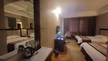 A hotel room with a large mirror, a desk with a kettle, two beds, a small table, and a chair.
