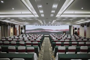 Un salón de conferencias con filas de sillas, una pantalla grande al frente y piso alfombrado.