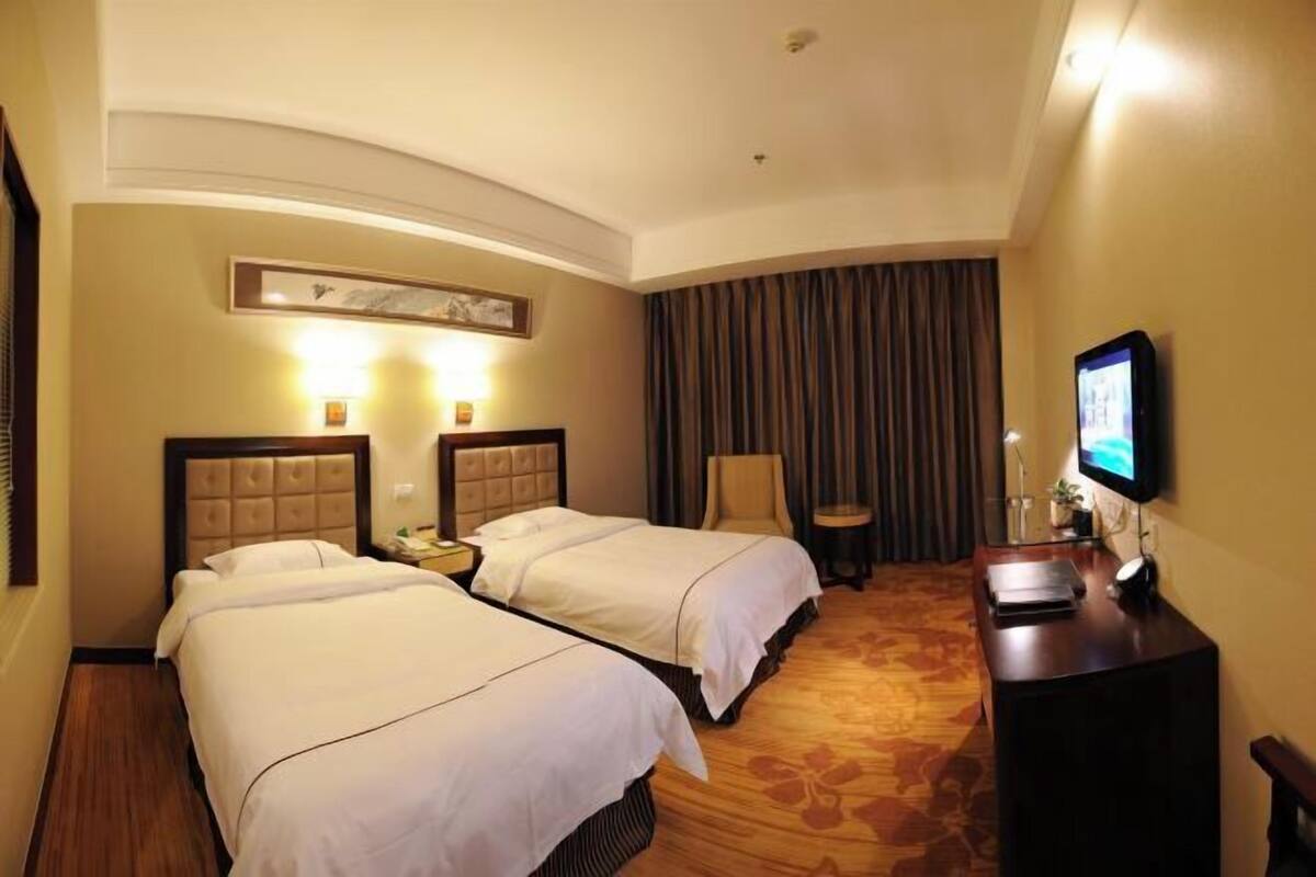 Een hotelkamer met twee bedden, een bureau met een computer, een televisie en een raam met gordijnen.
