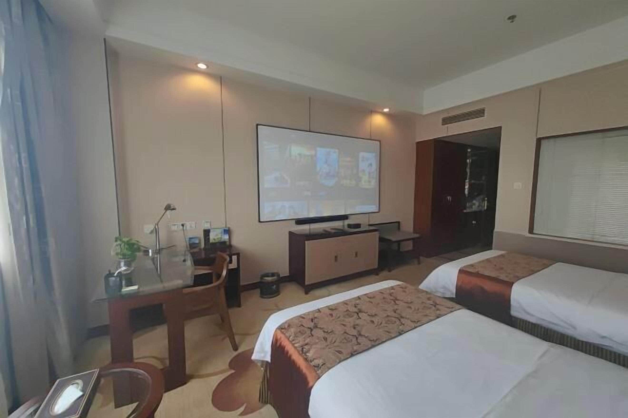 Habitació d'hotel amb un llit, un escriptori amb un ordinador, una televisió i una finestra.
