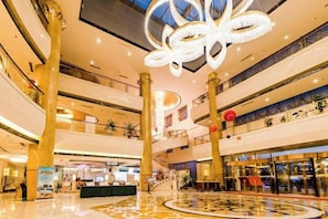 A multi-level shopping mall with a central atrium, escalators, and a decorative ceiling light fixture.