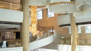 Un amplio atrio con varios niveles, una imponente escalera y candelabros ornamentales.