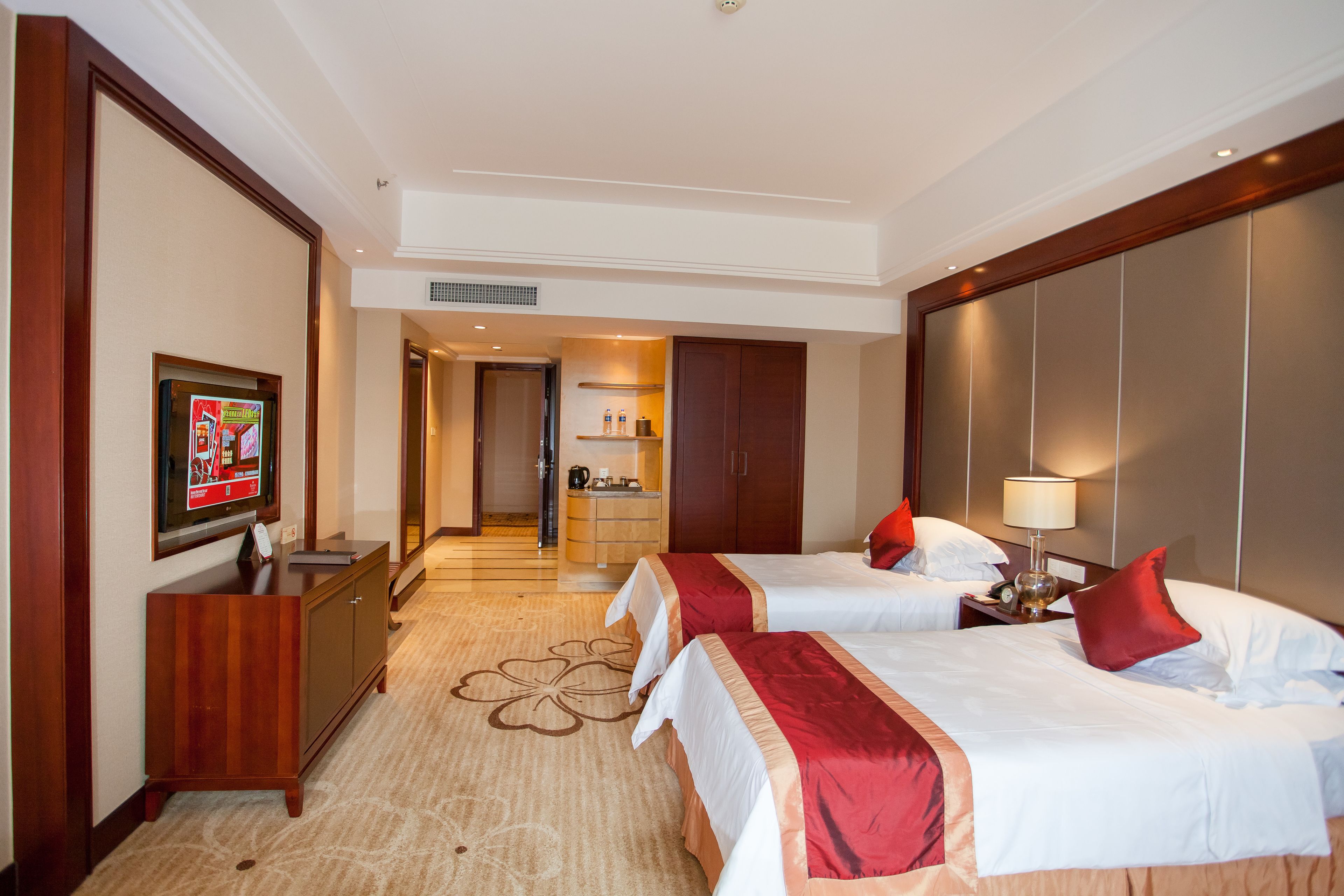Une chambre d’hôtel avec deux lits, une télévision, un bureau et une salle de bain visible à travers une porte ouverte.