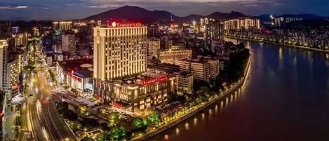 Un hotel de altura con un letrero llamativo, ubicado junto a un río y un paseo marítimo bien iluminado.