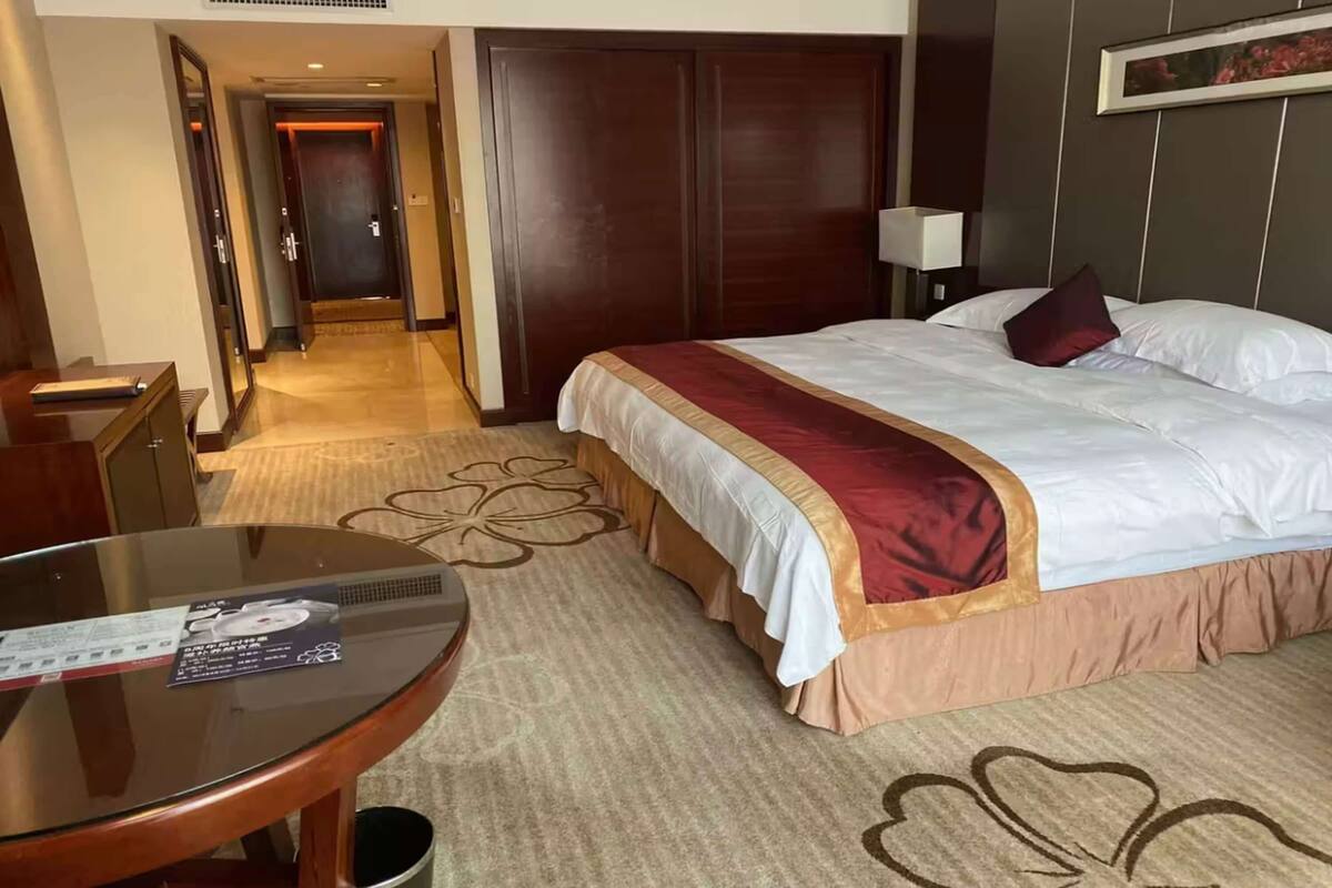 Una habitación de hotel con una cama, una mesa redonda de vidrio, un escritorio de madera y un armario.