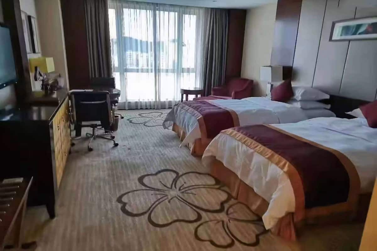Habitación de hotel con dos camas, un escritorio, una silla y un ventanal con cortinas.