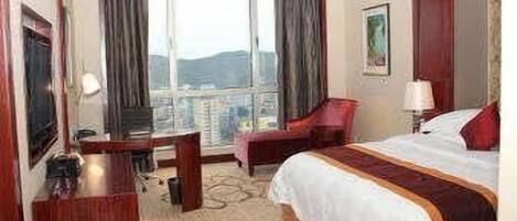 Ein Hotelzimmer mit einem Bett, einem Schreibtisch, einem Sessel, einem Fernseher und einem Vorhangfenster.