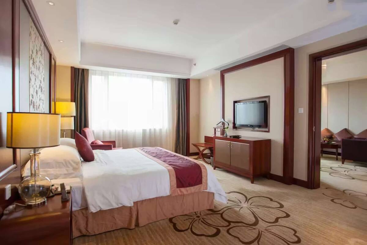Habitación de hotel con una cama grande, un escritorio, un televisor y vista a otra habitación.