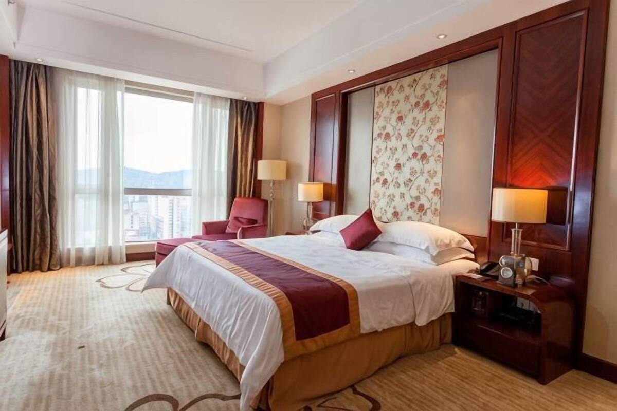 Habitación de hotel con una cama grande, dos mesitas de noche, una silla, un escritorio y vistas a la ciudad.