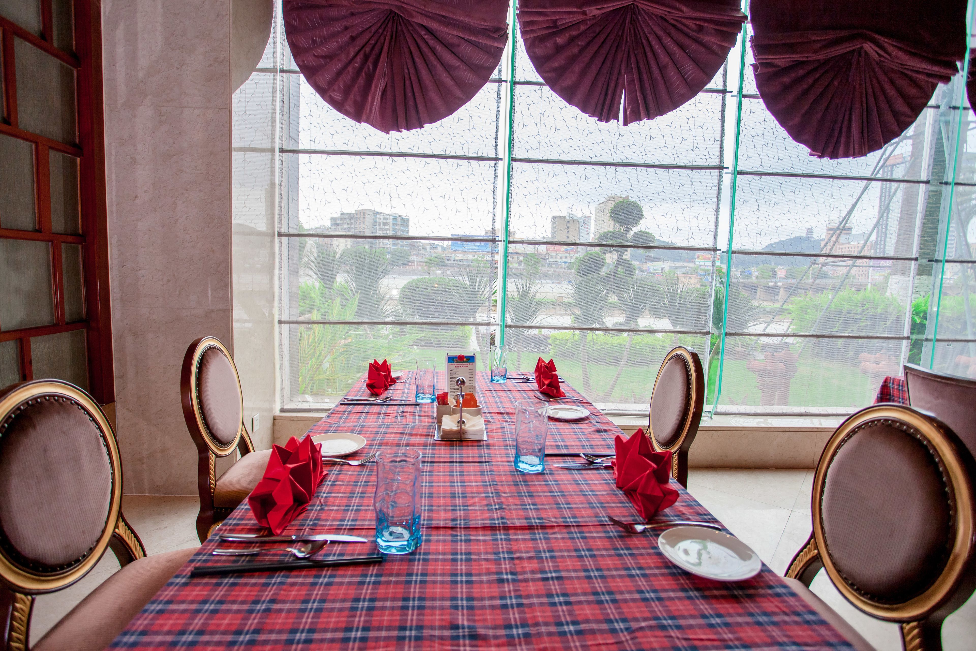 Une table à manger dressée pour quatre personnes, avec une nappe à carreaux rouges et bleus, des serviettes rouges et de la vaisselle transparente.