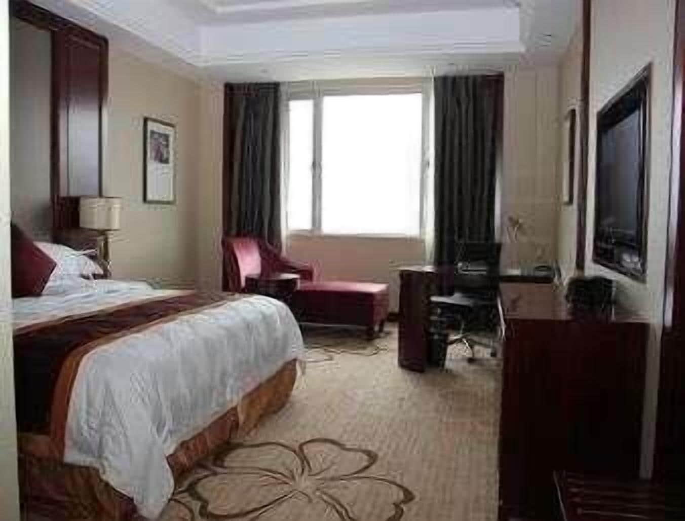 Una habitación de hotel con una cama grande, un escritorio con silla, televisión y ventana con cortinas.