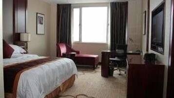 Una habitación de hotel con una cama grande, un escritorio con silla, televisión y ventana con cortinas.