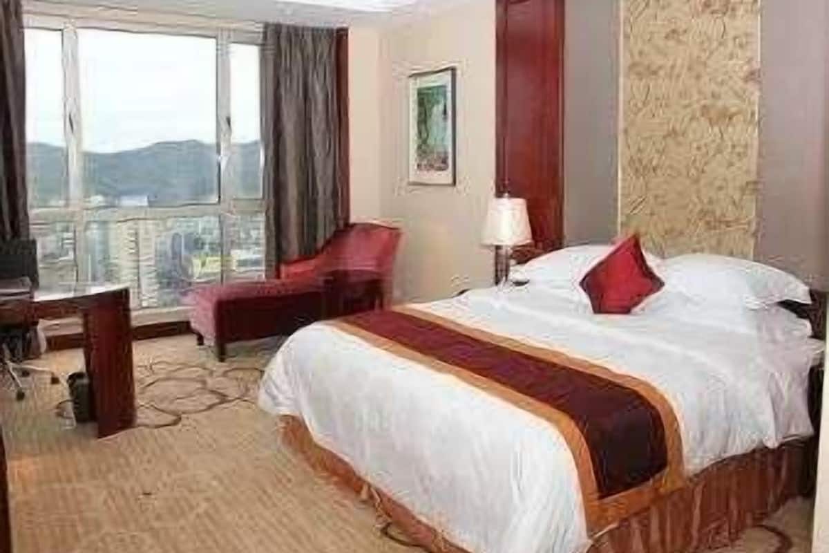 Habitación de hotel con una cama grande, un escritorio, una silla y una ventana con vistas a la ciudad.